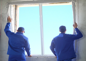 Two men in working clothes set new window frame into the window opening