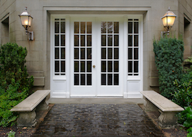Elegant stone walkway bordered by stone benches leading to a double glass paned front door with two